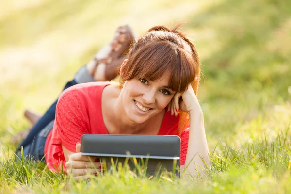 Menina morena bonita na grama está olhando uma tela digital — Fotografia de Stock