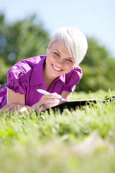 Hermosa estudiante femenina está estudiando en un campo verde —  Fotos de Stock