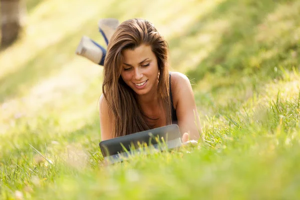 Hübsches brünettes Mädchen auf dem Gras sucht einen digitalen Bildschirm — Stockfoto