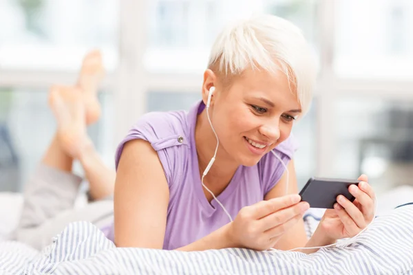 Young woman phoning in the bed with headphones — Stock Photo, Image