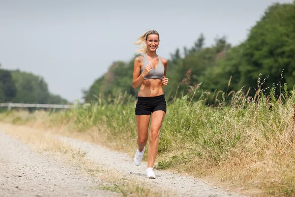 Beautiful blonde woman running along the riverside — Stock Photo, Image