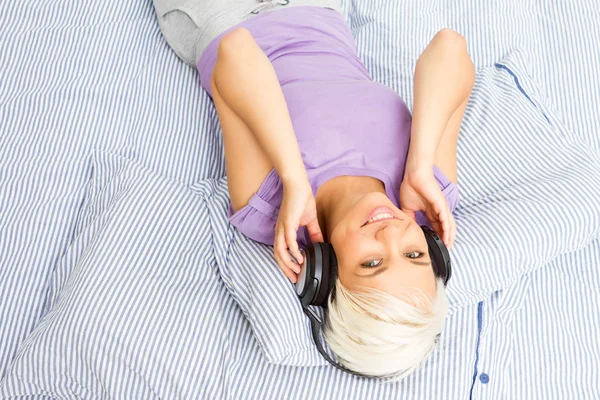 Mujer rubia escuchando música con auriculares en la cama —  Fotos de Stock