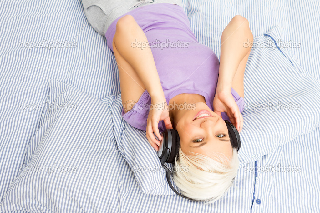 Blonde woman listening to music with headphones in the bed