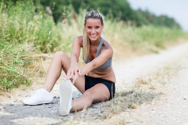 Smiling blonde woman is stretching on a field street — Stock Photo, Image