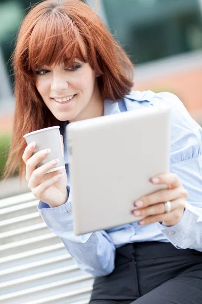 Geschäftsfrau trinkt einen Kaffee, während sie auf den Tablet-PC schaut — Stockfoto