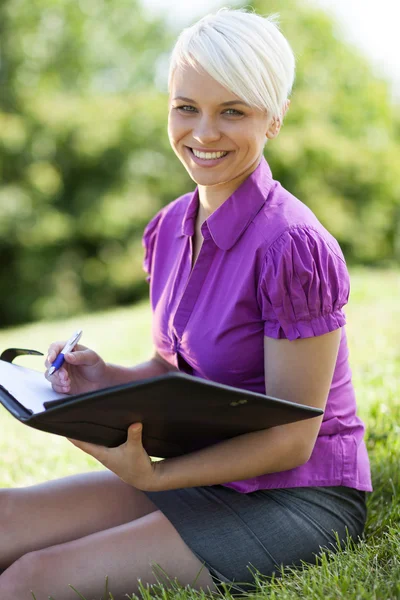 Smiling blond woman sitting in a park — Stock Photo, Image