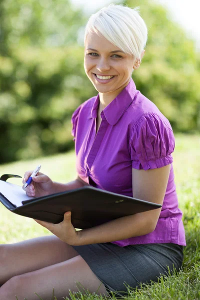 Sorrindo mulher loira sentada em um parque Imagens Royalty-Free