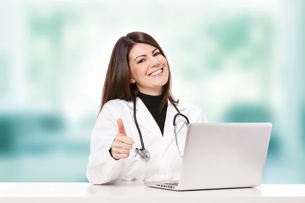 Female doctor sitting at her desk and smiling — Stock Photo, Image