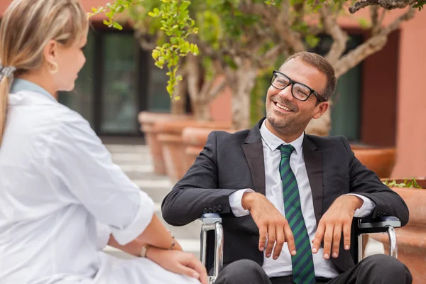 Homme d'affaires souriant en fauteuil roulant regardant vers son médecin — Photo