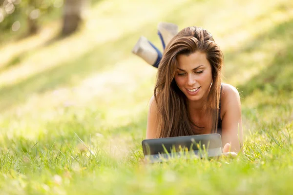 Mooie brunette meisje op het gras naar op zoek is een digitaal scherm — Stockfoto