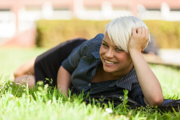 Bionda donna sorridente sdraiata su un campo di erba — Foto Stock
