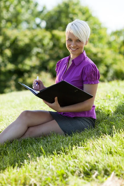 Femme blonde souriante assise dans un parc — Photo