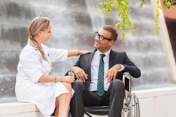 Femme médecin parle à un homme d'affaires en fauteuil roulant — Photo