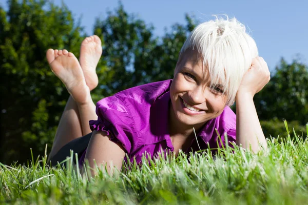 Blonde Smiling woman laying on a grass field Stock Photo