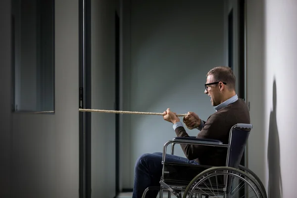 Koncepcyjne zdjęcie człowieka na wózku inwalidzkim jest ciągnięcie liny symboliz — Zdjęcie stockowe