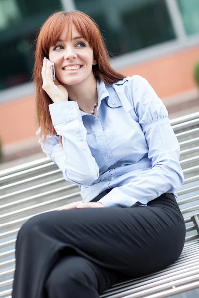 Geschäftsfrau mit roten Haaren sitzt auf einer Metallbank und telefoniert — Stockfoto