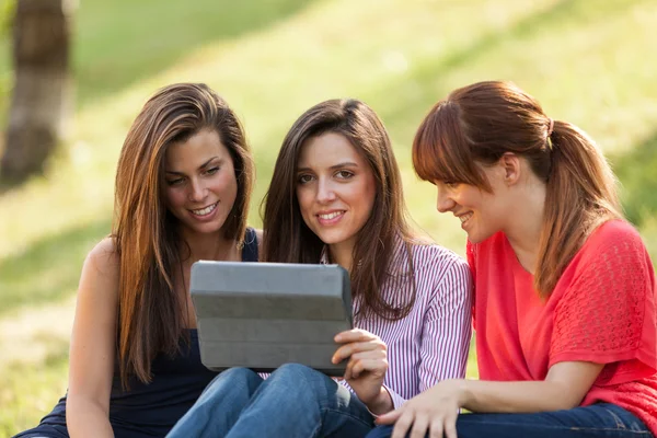 Tři ženy sedí na trávě a při pohledu na digitální tablet — Stock fotografie