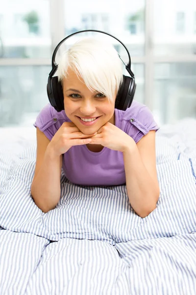 Femme blonde écoutant de la musique avec des écouteurs dans le lit — Photo