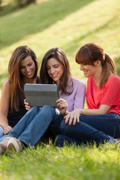 Drie vrouw op gras zitten en kijken naar een digitale tablet — Stockfoto