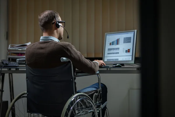 Hombre en silla de ruedas está trabajando hasta tarde en la oficina — Foto de Stock