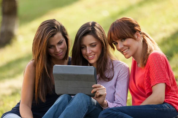 Três mulheres sentadas na grama e olhando para um tablet digital — Fotografia de Stock