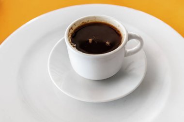 Kafeteryadaki parlak turuncu bir masanın üstünde fincanda koyu ve kokulu bir kahve.