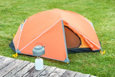 Kamp alanında turuncu çadırı olan bir gaz ocağında çaydanlık. Soba, ateş yakmak yerine çevre dostu ve güvenli yemek pişirmek için kullanılıyor.