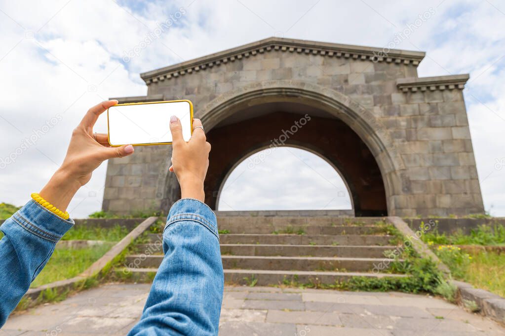 Blogger woman with blank isolated smartphone screen taking photos of the landscape near the Charents Arch in Armenia near Yerevan