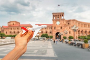 Tourist woman with a toy airplane on the background of a Republic Square in Yerevan. Concept of air flight transportation in Armenia clipart