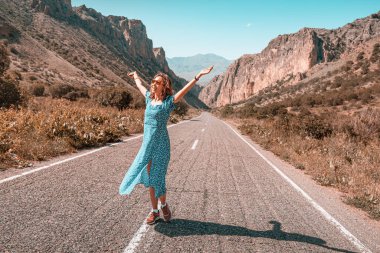 Elbiseli mutlu bir kadın, dağlık bir bölgede asfalt yolda yürürken eğleniyor ve kaygısızca yürüyor. Özgürlük ve Gençlik psikolojisi kavramı