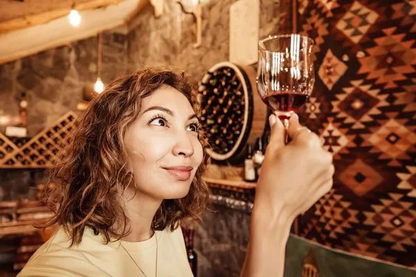 An Asian woman tastes and analyzes wine in the cellar of a local winery. Concept of tours and sommelier work