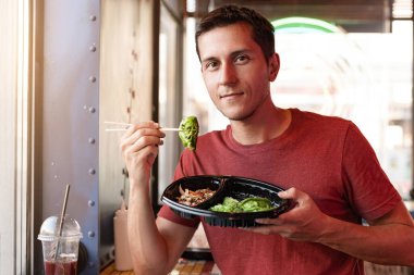 Pencerenin yanındaki fast food restoranında Asya usulü Çin mantısı yiyen mutlu bir adam.