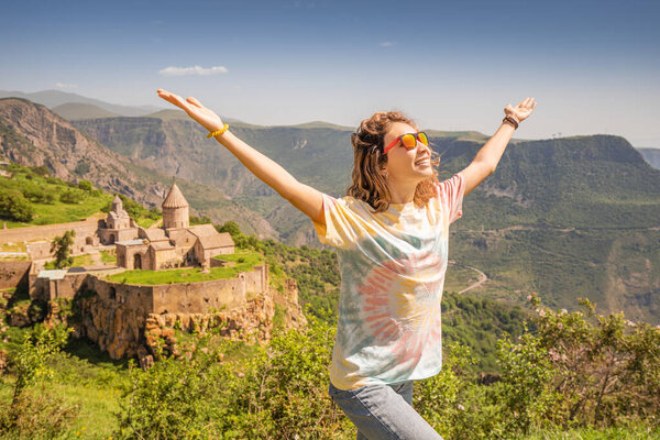 Happy traveler girl raised her hands and rejoices wonderful view of the main tourist attraction of Syunik and South Armenia - Tatev monastery