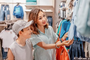 Anne ve oğlu alışveriş merkezindeki mağazadan almak için kıyafet seçiyorlar. İlişkiler, annelik ve çocukluk seçimleri.