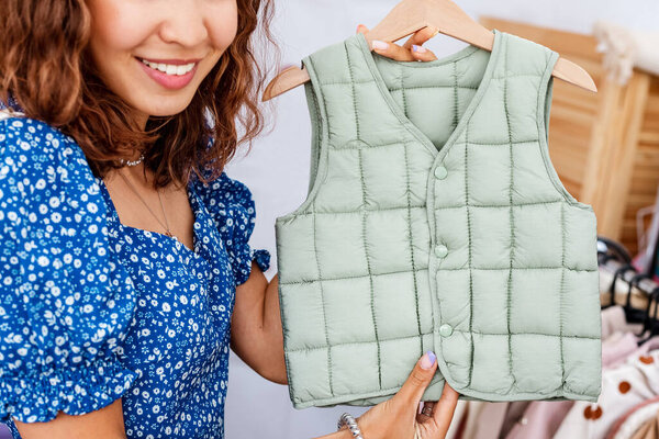Счастливая женщина выбирает стильный бронежилет для дочери в бутике с коллекцией детской одежды. Концепция магазинов и материнства