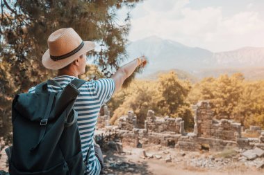 Mutlu gezgin, Türkiye 'deki Tahtali Dağı manzaralı antik Yunan kenti Phaselis' teki antik bir amfi tiyatronun kalıntılarını keşfediyor.