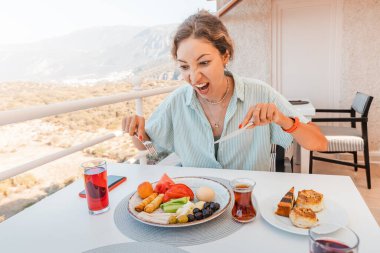 İştahlı bir kadın otelinin verandasında klasik bir Türk kahvaltısı yer.