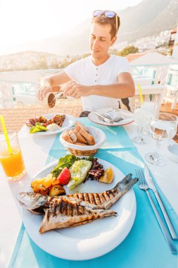 Happy man with grilled seabass fish and other dishes in a seafood restaurant. The Mediterranean diet and epicure lifestyle concept