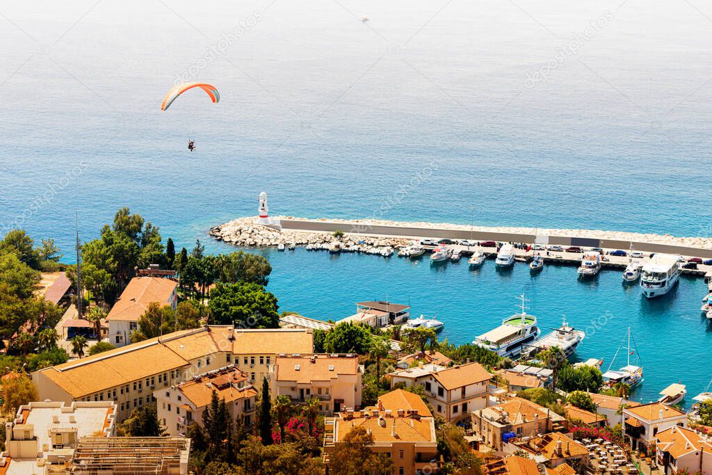 Charming view of the seaside resort town of Kas in Turkey. Romantic lighthouse at the entrance to the port and a paraglider flies over the marina
