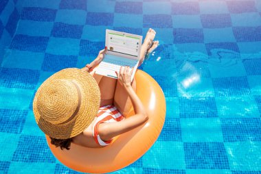 Yüzme havuzunda şişme mayo giymiş bir kadın ve dizüstü bilgisayarındaki internet sitelerinde sörf yapıyor. Boş bir hafta sonu ve uzak serbest çalışma konsepti