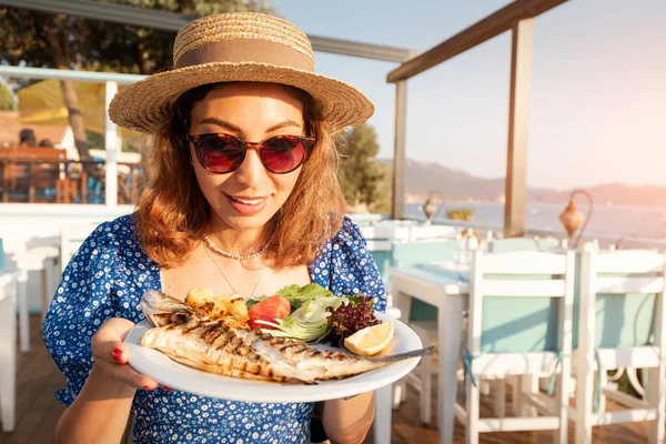 Deniz ürünleri restoranında fırında levrek pişiren mutlu bir kadın. Akdeniz diyeti, Omega-3 yağ ve vitaminlerinin vazgeçilmez bir kaynağıdır.