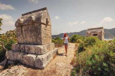 Türkiye 'de Kekova adası yakınlarındaki büyüleyici lahit ve mezarlarla Lycian mezarlığının antik kalıntılarını araştıran bir gezgin kız. Tarihi görüntüler ve arkeoloji kavramı