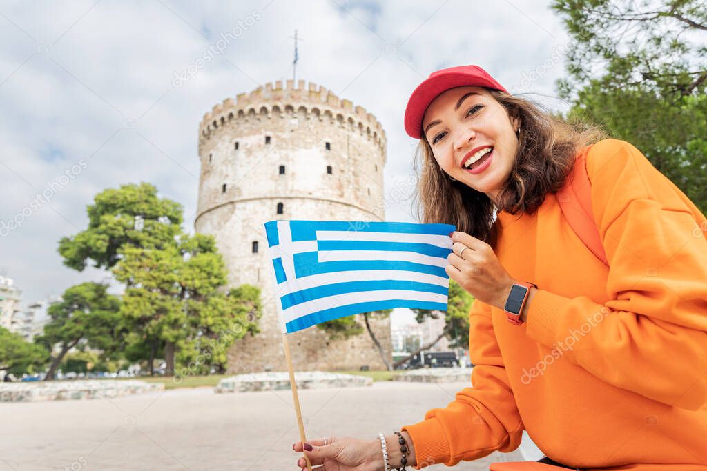 Happy student girl with a Greek flag on the background of a White Tower in Thessaloniki. The concept of citizenship or learning Greek language in university