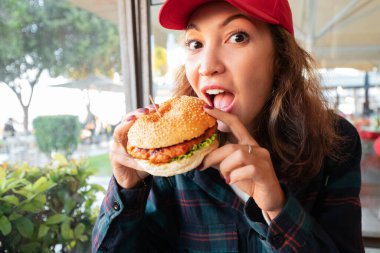 Gülümseyen Asyalı kız fast food restoranında büyük bir hamburger ve patates kızartması yiyor.