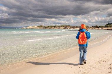 Sırt çantalı yalnız bir kız deniz kıyısında bir patika boyunca yürüyor. Sezon dışında yürüyüş ve aktivite kavramı.