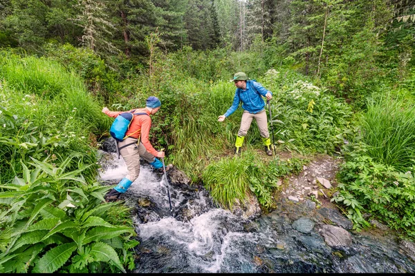 A man helps a girl to jump or ford over a mountain stream on a hike. Travel and outdoors concept