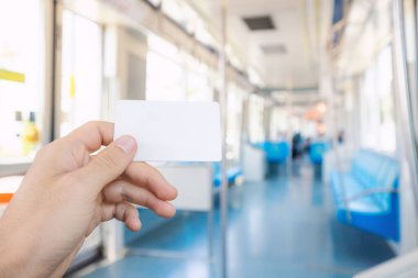 Şehirdeki modern kentsel ulaşım sistemi için ulaşılamaz ve nakitsiz para ödeyen beyaz kart tutan bir yolcunun eli. Metro ya da tramvay vagonunun içi.