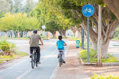 19 Mayıs 2022, Antalya, Türkiye: Bisikletçiler baba ve oğlu, boyalı asfalt ve yol işaretleri olan bir parkta bisiklet yoluna çıktılar. Şehirdeki çevre dostu ulaşım altyapısı ve güvenlik