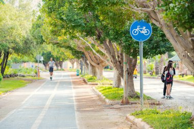 19 Mayıs 2022, Antalya, Türkiye: Bisikletçiler ve scooterlar, boyalı kaldırım ve yol işaretleri olan bir parkta bisiklet yolu boyunca seyahat ediyorlar. Yakınlarda yürüyen yayalar.
