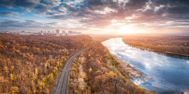 Şehrin banliyölerinde demiryolunun havadan manzaralı manzarası. Gün batımının görkemli bulutları nehir sularına yansıyor.